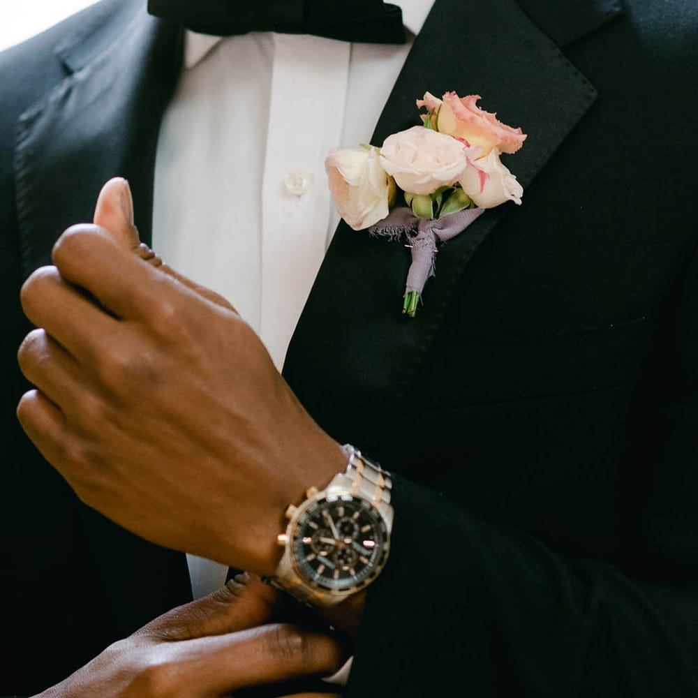Groom wears black tie for the wedding with a pink flower buttonhole tied with purple ribbon 