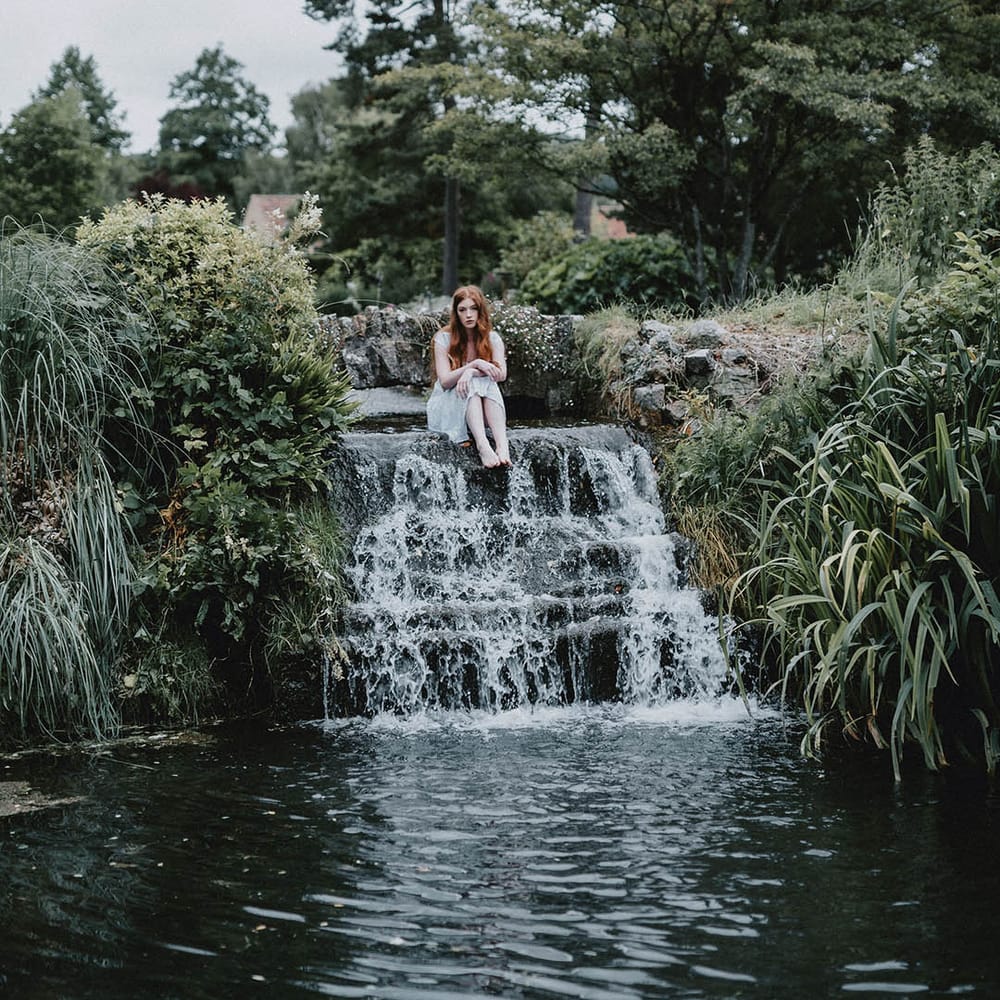 Beautiful bride with long hair and natural makeup sitting in the moat at Bishop's Palace, Wells