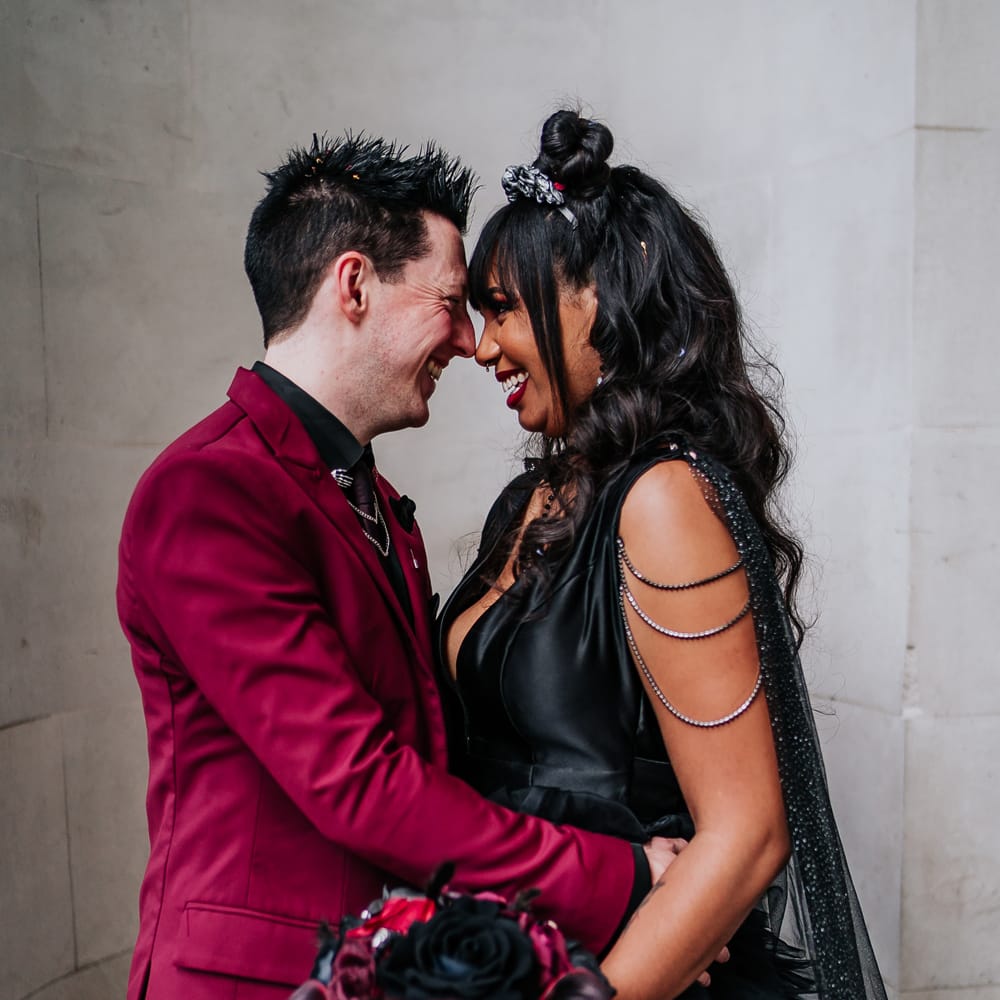 Bride in black wedding dress & groom embrace on their wedding day outside the Old Marylebone Town Hall