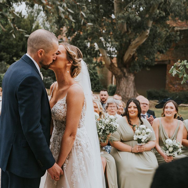 The bride and groom share their first kiss as a married couple at their outdoor wedding ceremony
