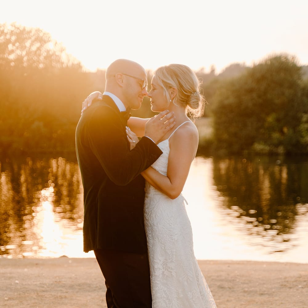 Bride wears lace fitted wedding dress as she embraces her groom outdoors during golden hour couples portraits