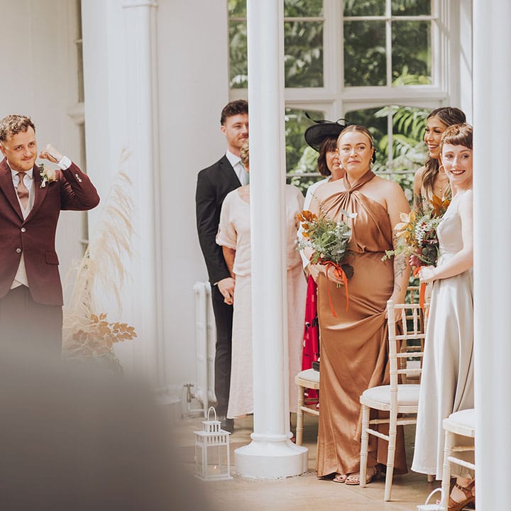 Groom wears maroon suit with grey waistcoat and floral buttonhole 