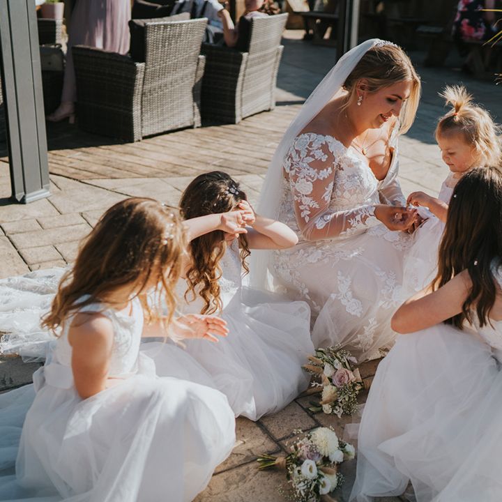 Bride sits with flower girls outdoors on her wedding day at Watermouth Cove 