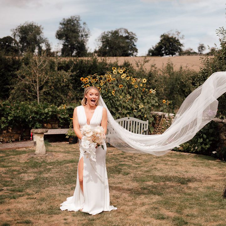 Bride wearing a satin wedding dress with deep plunge and cathedral length veil with a bridesmaid in a brown satin dress 
