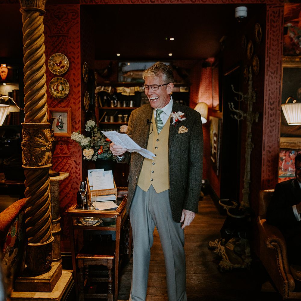 Father of the bride wearing dark grey blazer, grey trousers, yellow waistcoat, green tie and autumnal boutonniere giving a speech at intimate London wedding
