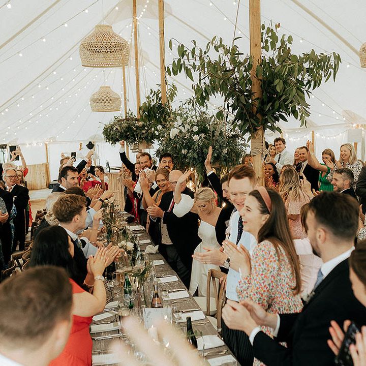 Wedding guests celebrate in marquee complete with hanging floral installations 