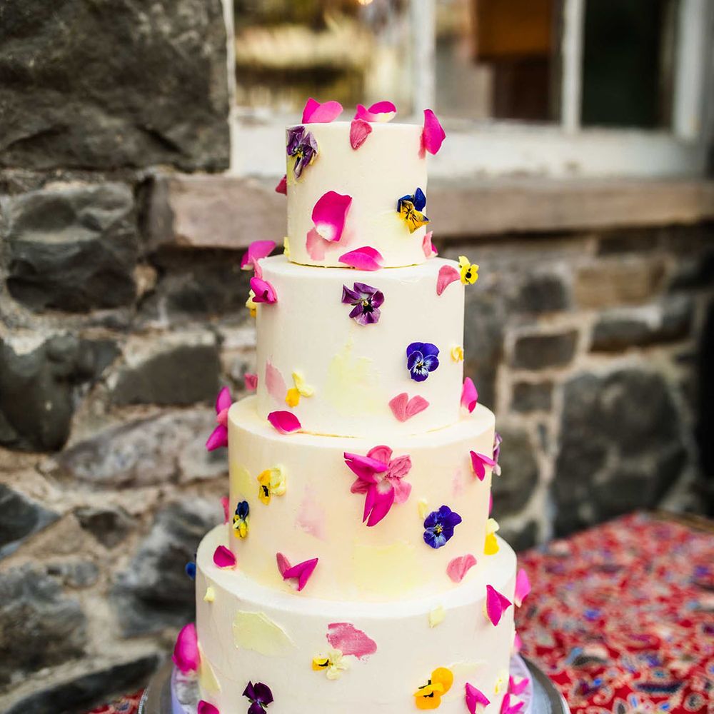 White frosted four tier wedding cake complete with colourful pressed petals 