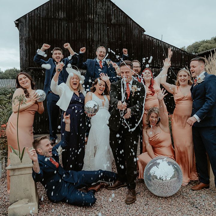Champagne popping photo of the bride and groom celebrating with their wedding party with disco ball wedding decor 