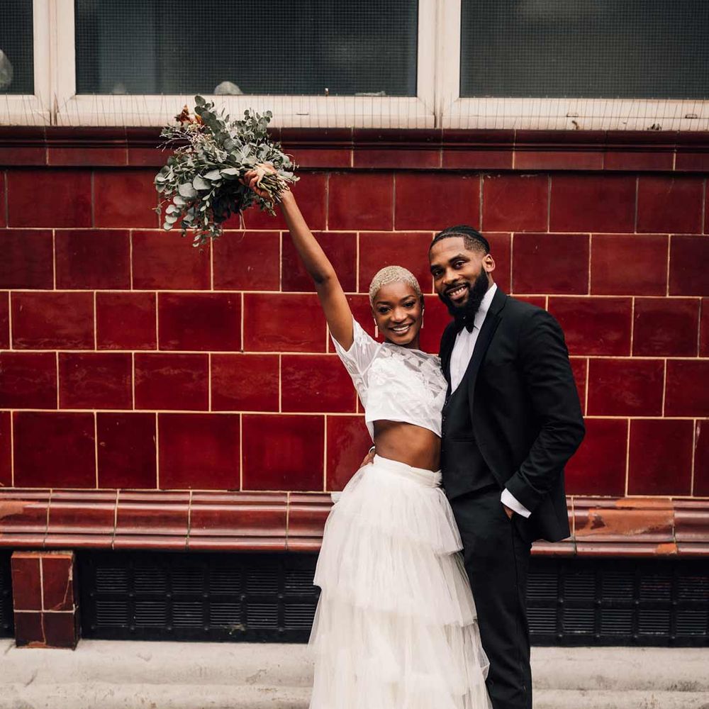 Bride in two piece bridal set with white short sleeve lace crop top and full tulle skirt standing with groom in classic black tuxedo 