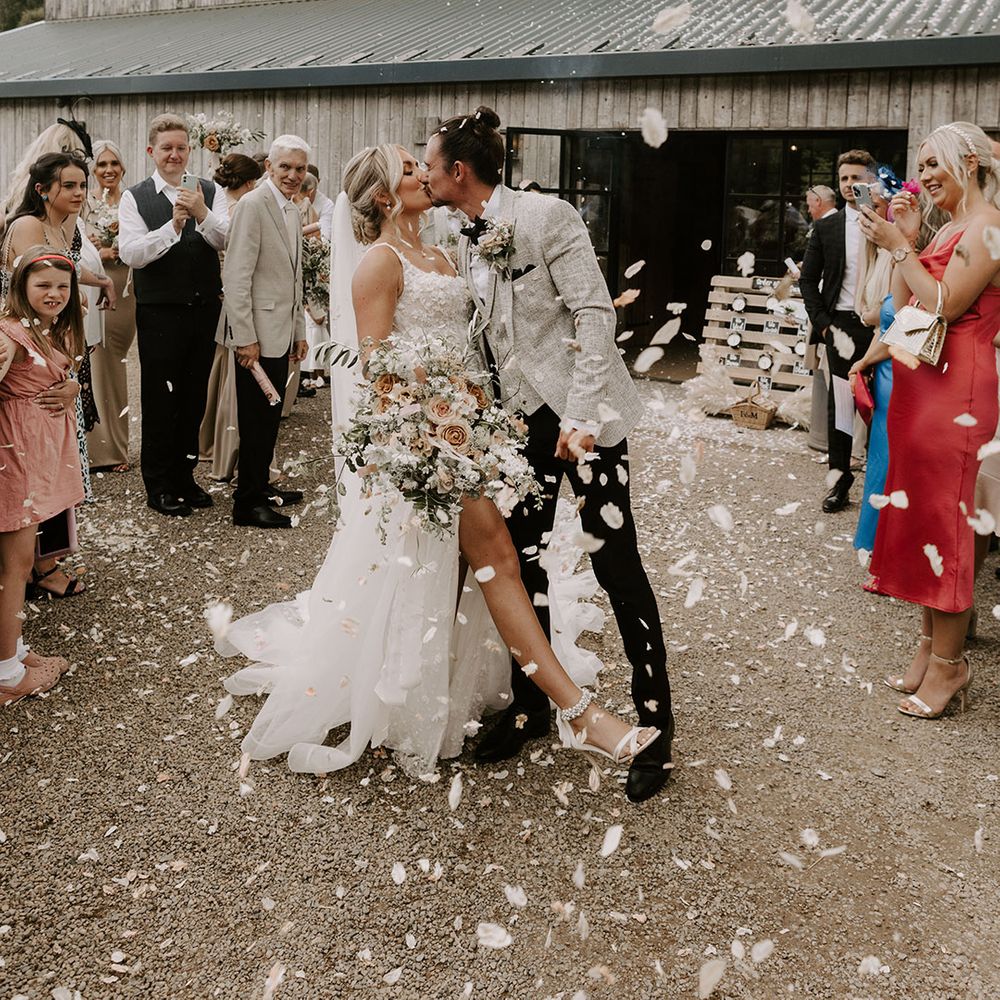 Bride in Eleganza Sposa wedding dress with split leg leans back and kisses the groom for the confetti exit after their ceremony 