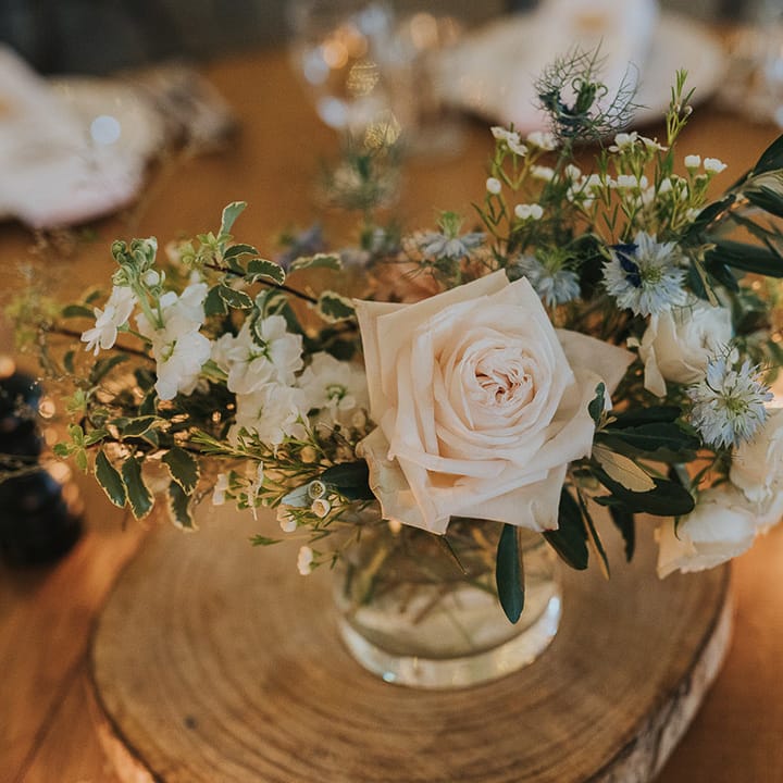 wedding centrepiece decor with pink rose and thistle flower stems in bottles on tree slices 