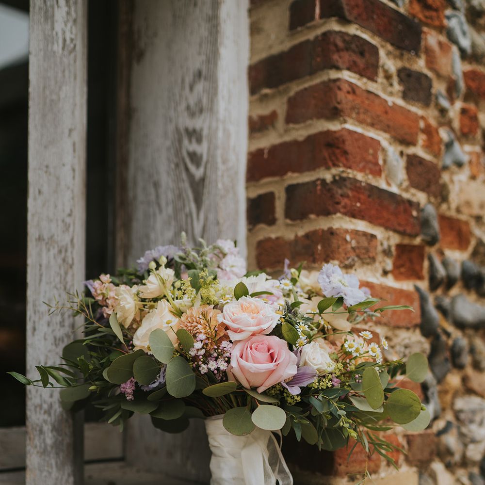 Bride's pink rose, daisy, purple and orange flower bouquet with foliage tied with white ribbon 