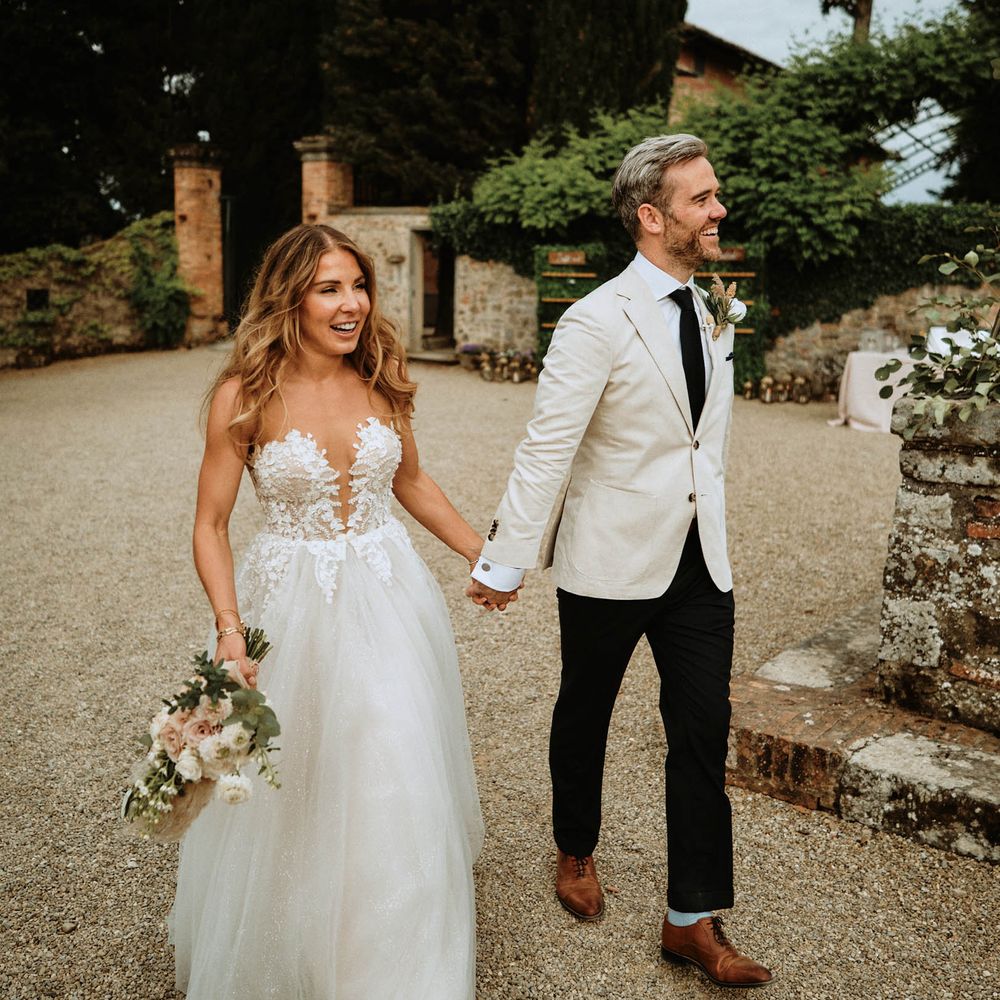 Bride and groom holding hands and smiling at italian wedding wearing a tulle wedding dress with embroidered bodice with groom in linen suit
