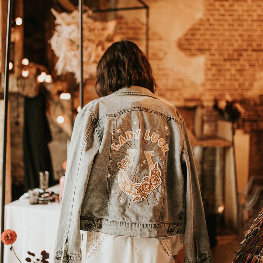 Bride in light wash wedding denim jacket with horse shoe badge and 'Lady Luck' 
