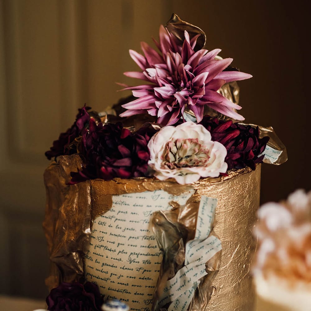 Gold iced wedding cake with newspaper print icing with purple flower decorations