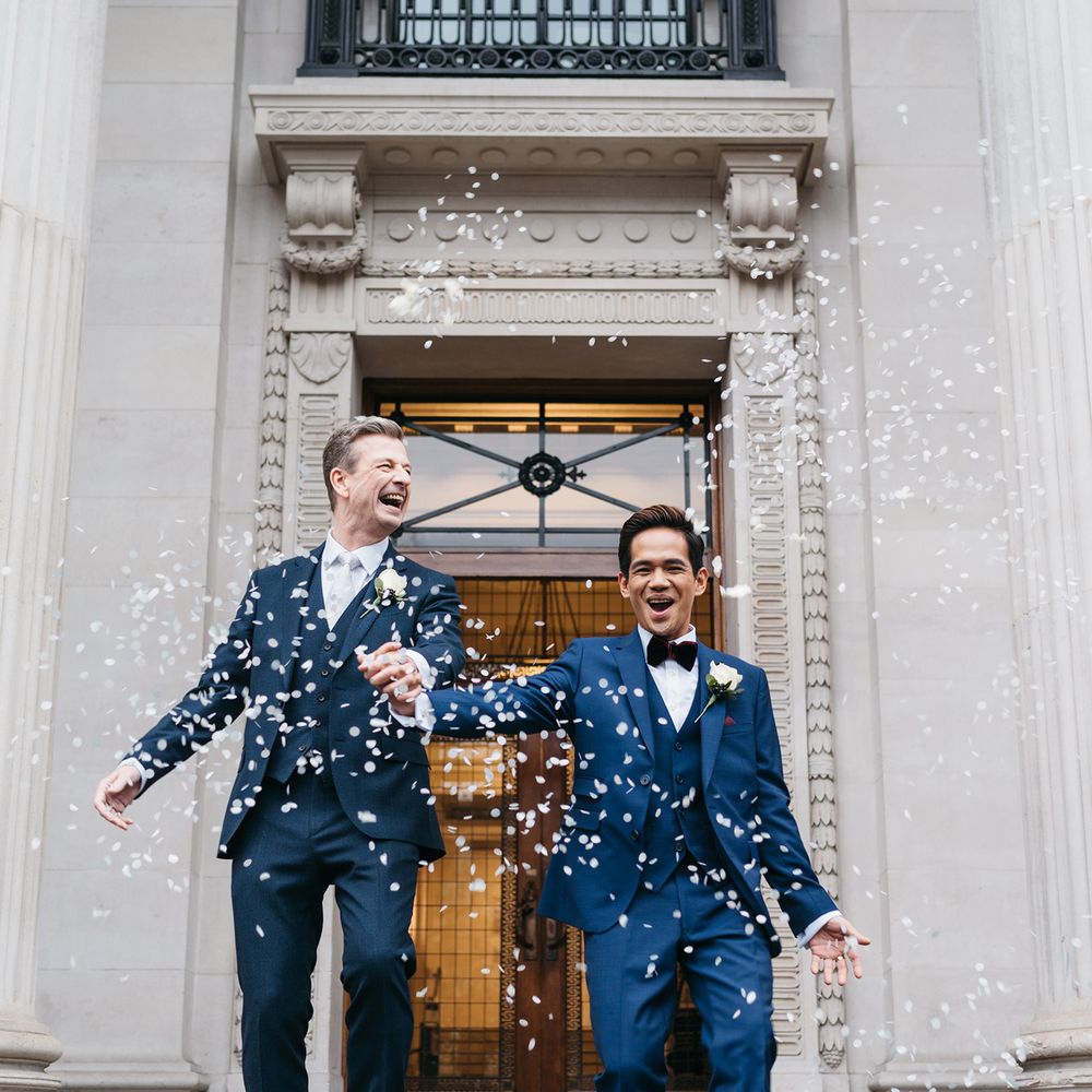 Grooms leave Old Marylebone Town Hall with confetti blowing in the wind as they celebrate