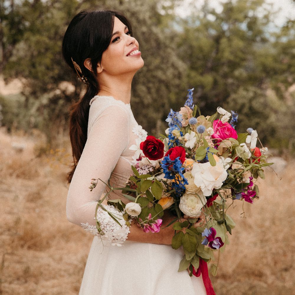 Bride laughs and tilts her head back holding bright and colourful bouquet 