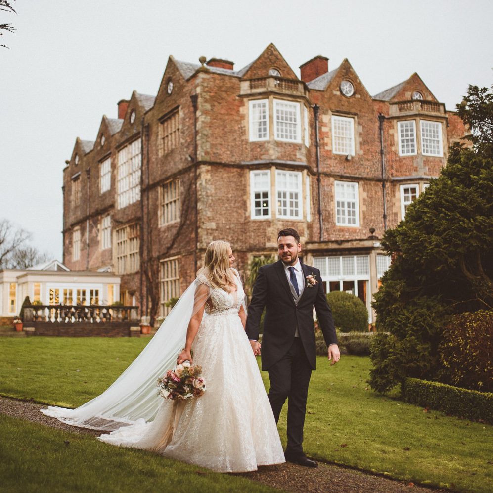 Bride in a princess wedding dress and groom in navy suit walking through the grounds at Goldsborough Hall 