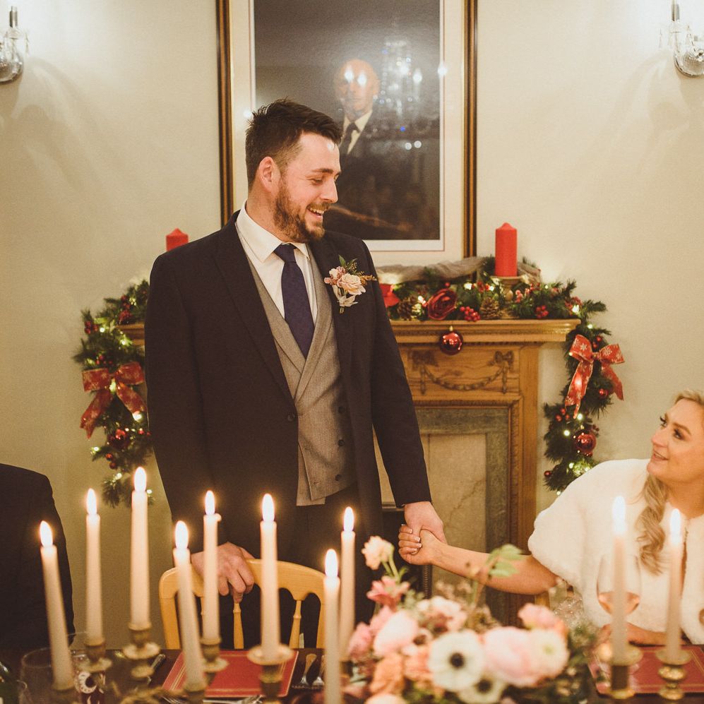 Groom in a navy suit with grey waistcoat holding hands with his bride during the wedding reception 