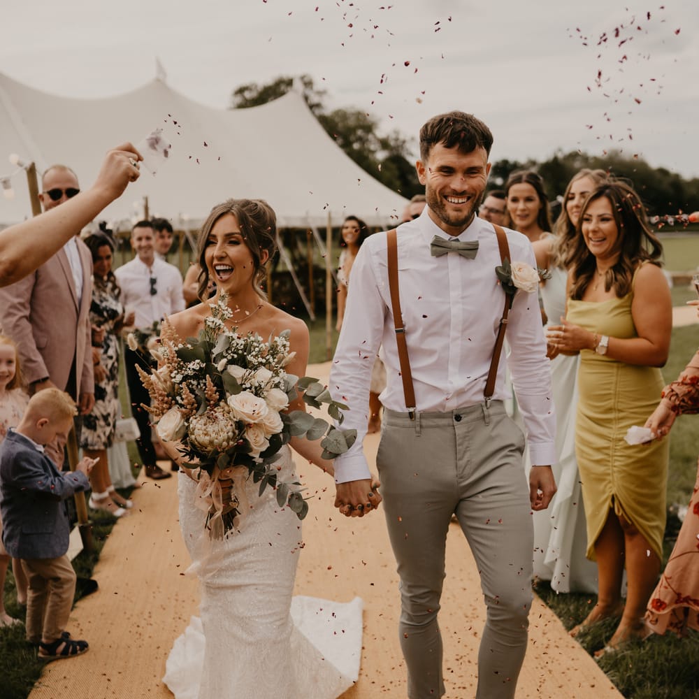 Bride & groom walk down the aisle at Duddon Mill Farm as wedding guests throw confetti around them | Mark Bamforth Photography
