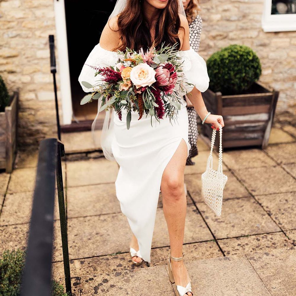 Bride in a strapless wedding dress with lace veil holding her wedding bouquet and a beaded bag