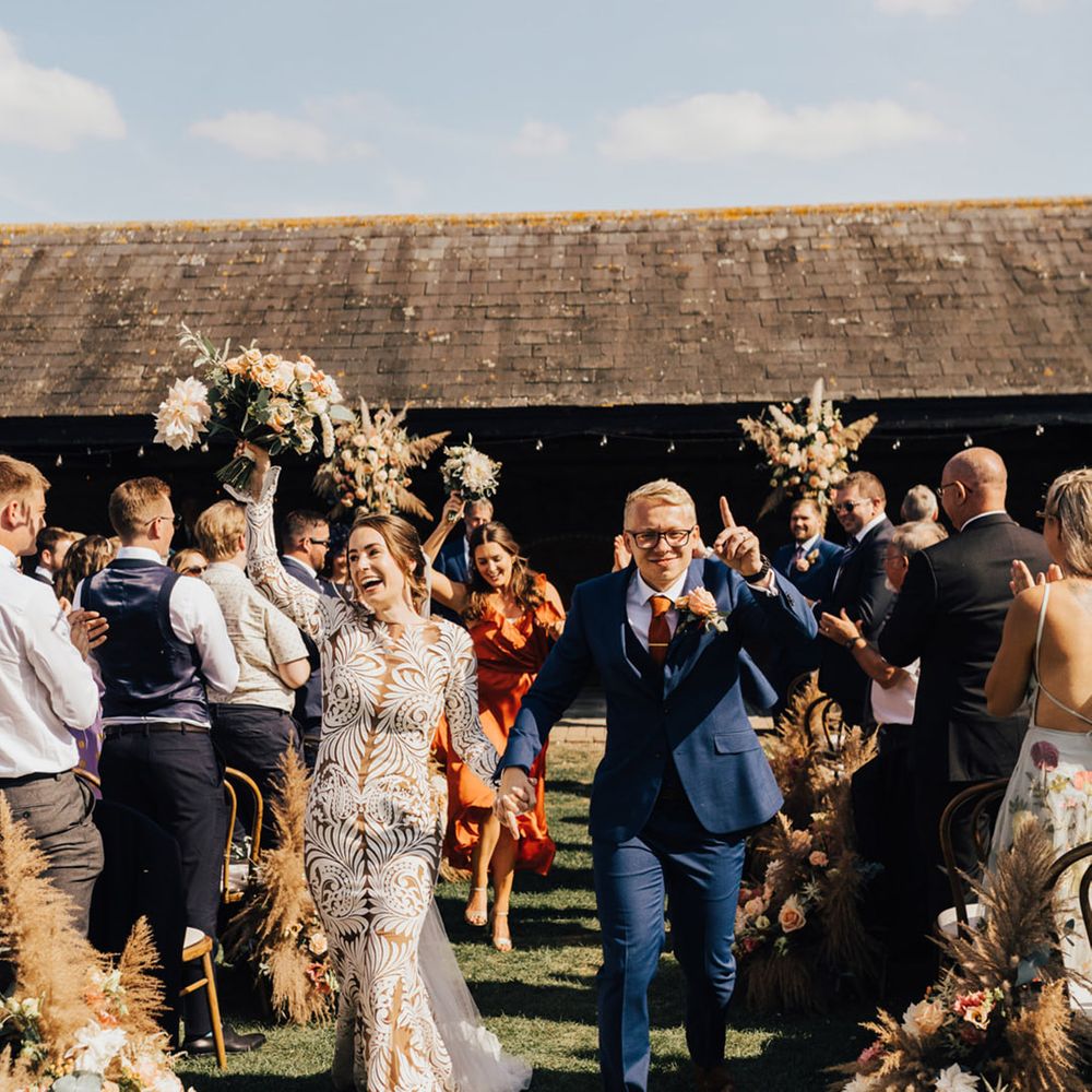 Boho Bride & Groom holding hands at Elmley Nature Reserve barn wedding with pampas grass arrangements