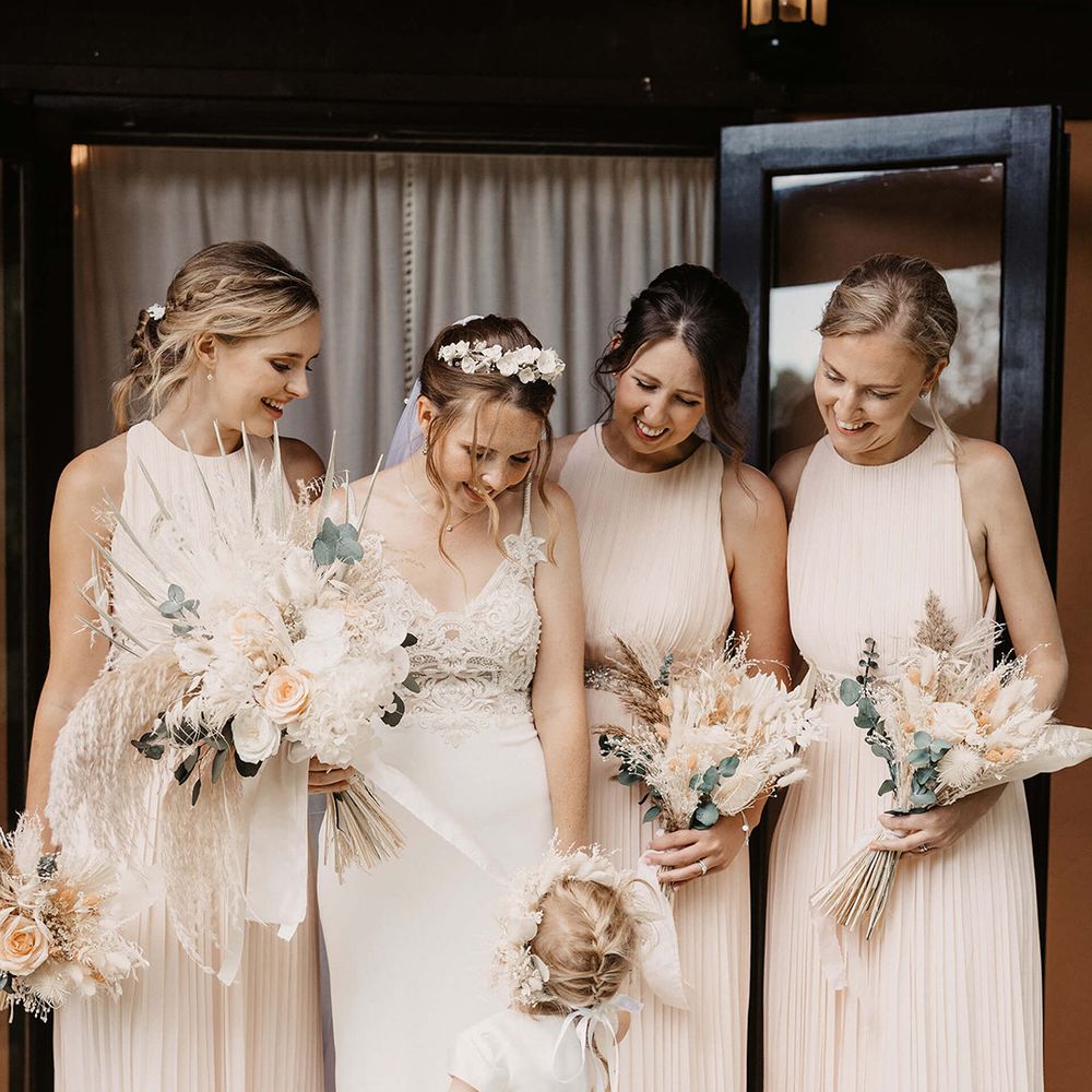 Bride stands with her bridesmaids who wear pale pink gowns as they smile lovingly at her daughter
