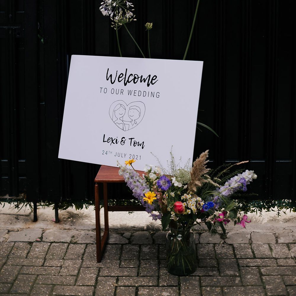 Simple welcome sign for wedding with personalised sketch, name and date with colourful flower bouquets