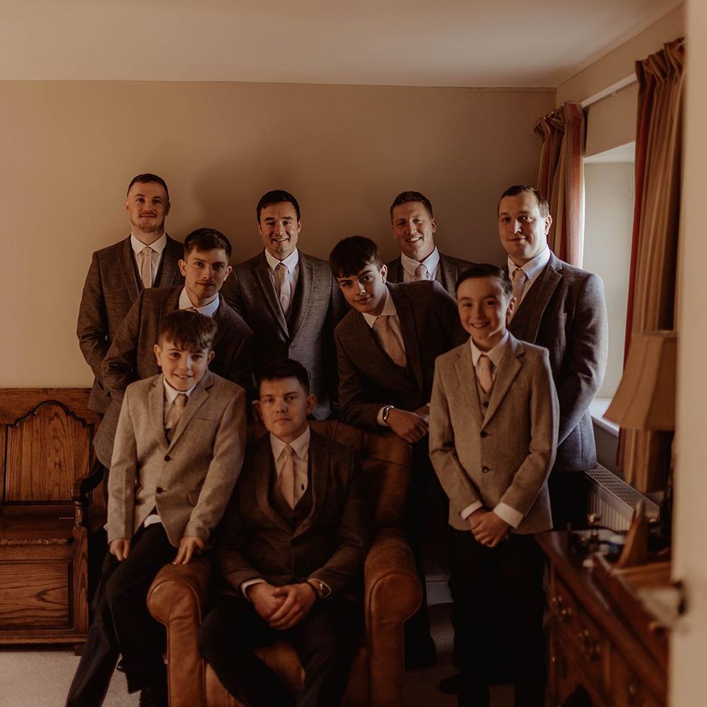 Groomsmen in brown three piece suits and rings bearers in lighter neutral suit for rustic barn wedding 