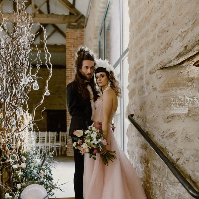 Bride in a pink strapless wedding dress by Felisiti Greis standing on the steps at The Tithe Barn Hooton Pagnell with her groom in a tuxedo 