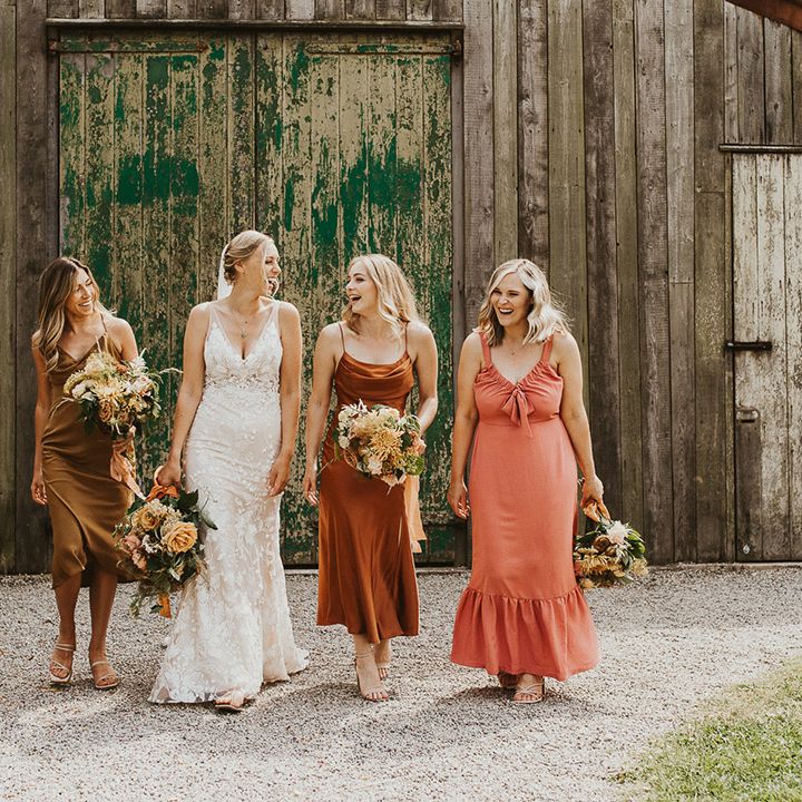 Bride in a lace Made With Love wedding dress standing with her bridesmaids in mismatched coloured dresses 