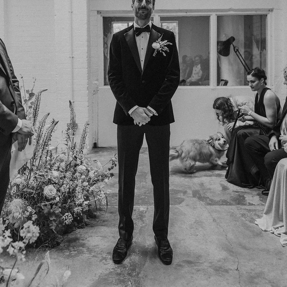 Groom in black tux with bow tie and boutonniere waiting for bride at the end of the alter at Hackney Studios