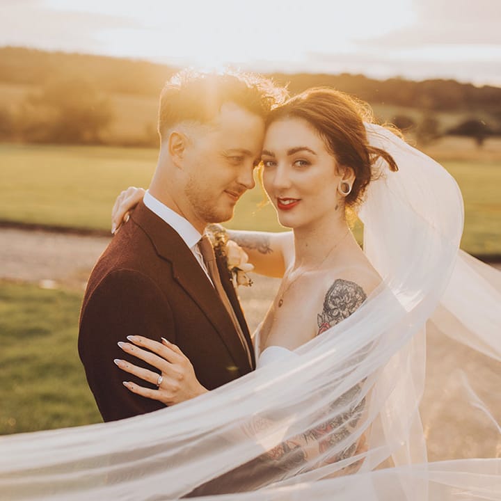 Bride's veil blows around herself and her groom during golden hour couples portraits