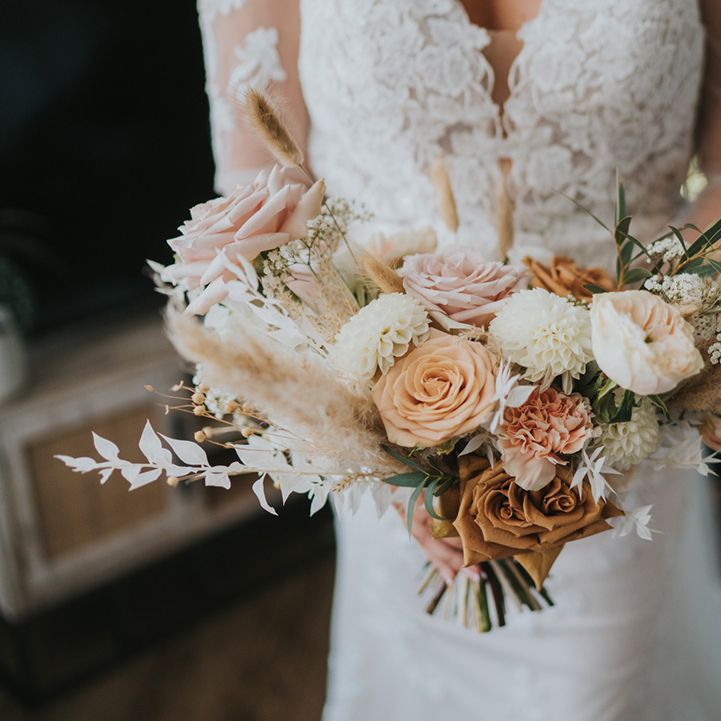 Bride in lace wedding dress holds pastel coloured bouquet 