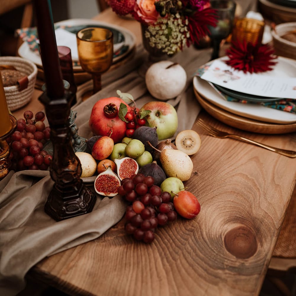 Seasonal fruit and vegetables decor on rustic autumnal wedding tablescape with large dark candlestick holders and dried flowers