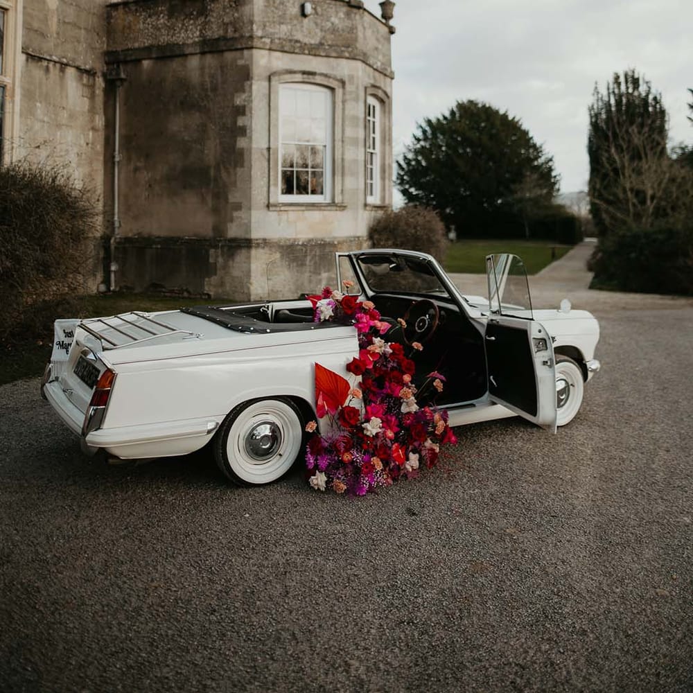 Off white classic convertible wedding car with red roses, off white peonies, lilac dried lowers, dahlias, orchids, roses and amaryllis decorations