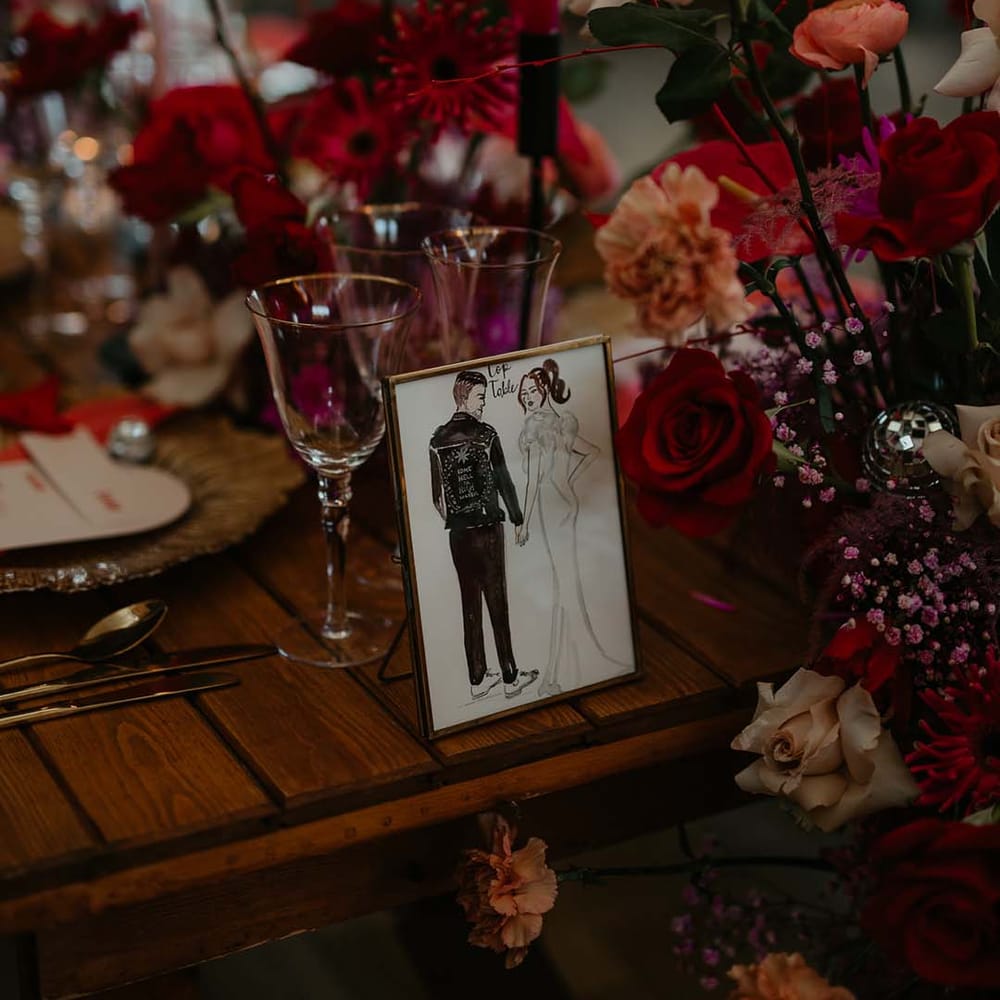 Personalised drawing of the couple in gold frame on magenta, disco themed wedding tablescape with red, off white and pink roses, magenta peonies, and red tapered candles 