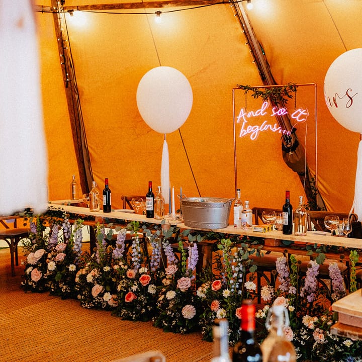 Tipi wedding reception with balloon wedding decor, neon lights and wildflowers decorating the top table 