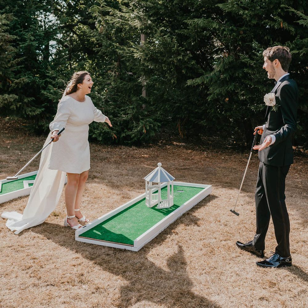 The bride in a patterned short wedding dress with bow and shoulder length veil playing wedding crazy golf with the groom in black tuxedo 