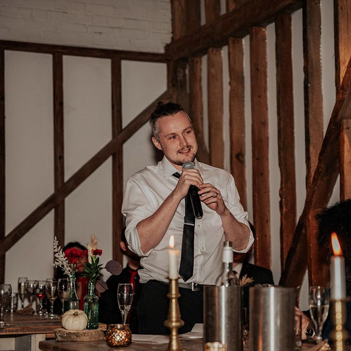 The groom stands up with a mircophone to read out his groom wedding speech with a man in a gorilla mask sitting next to him 