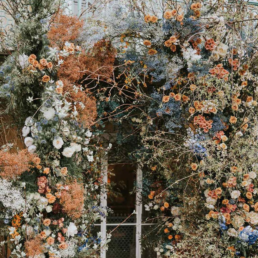 Large colourful flower arch with white garden roses, orange dried flowers, blue baby's-breath, eucalyptus, orange peonies and more 