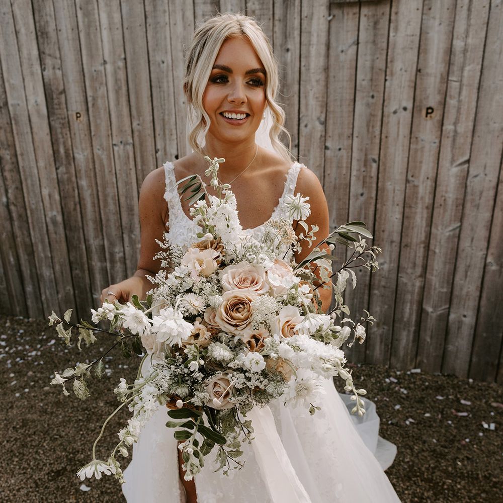 The bride in a floral wedding dress with split leg holding a big oversized neutral bridal bouquet with roses 