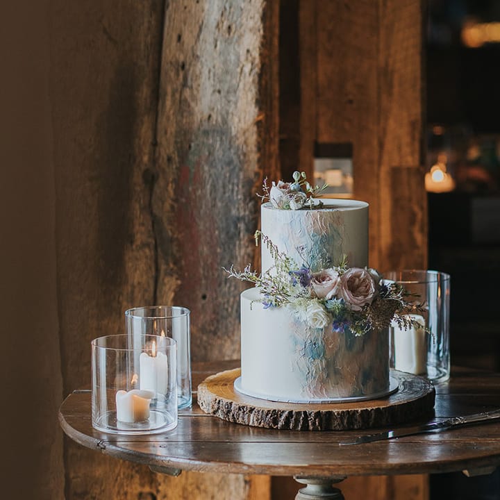two tier wedding cake on a tree slice with pastel design and wedding flowers 