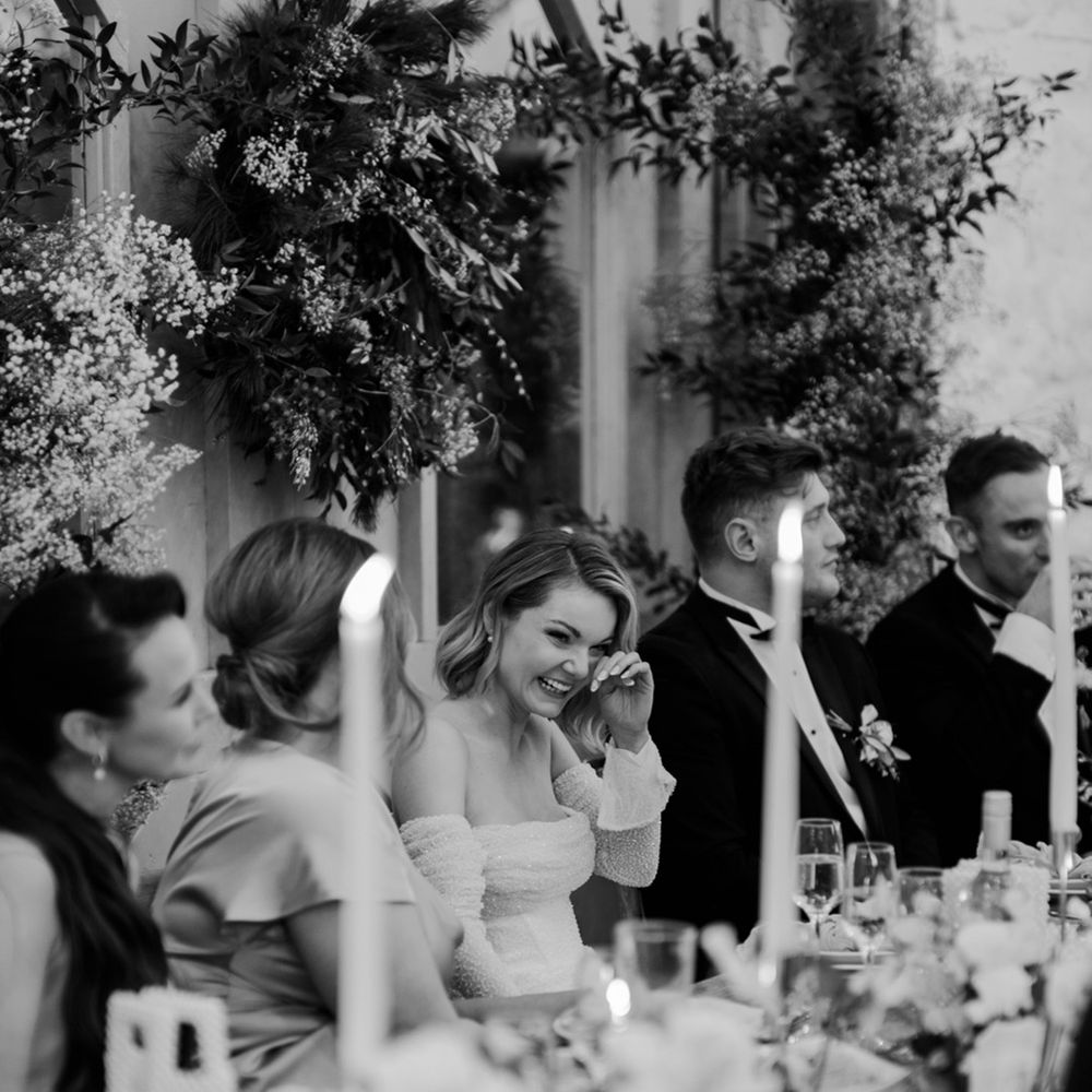 The bride laughs and wipes away tears as listens to the wedding speeches 