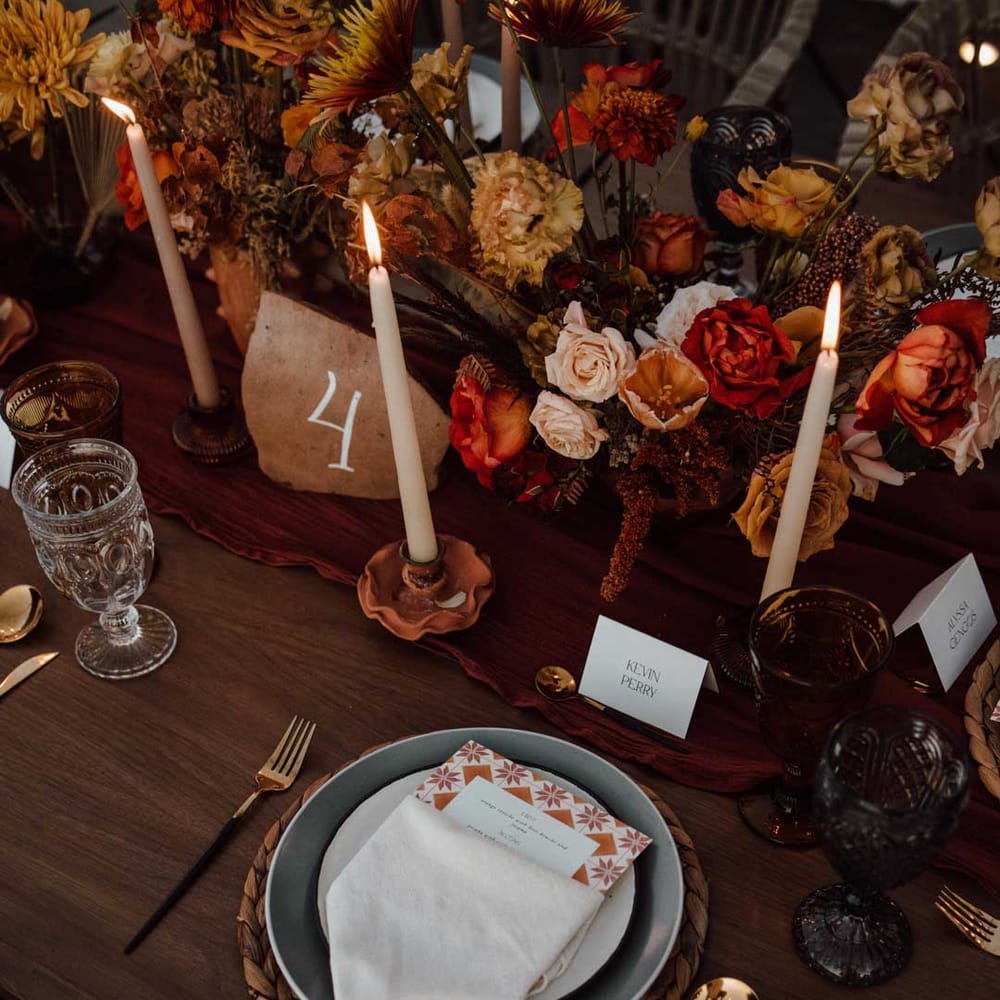 Rustic wedding tablescape with burnt orange dried roses, dried flower and foliage floral centrepieces, wooden slate wedding table numbers, light orange tapered candles and burnt orange table runners