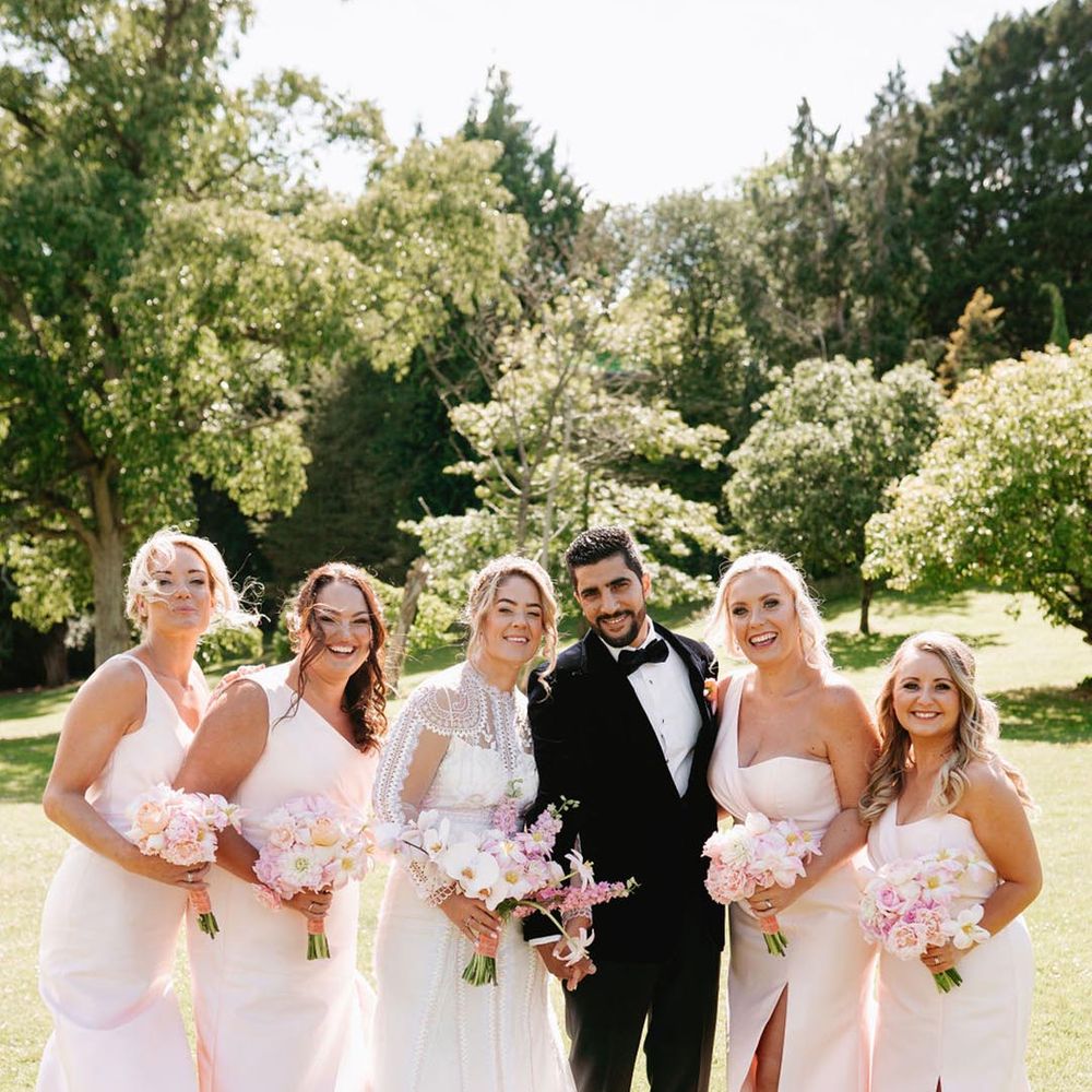 Bridal party in one shoulder pastel pink bridesmaid dresses with the bride and groom 