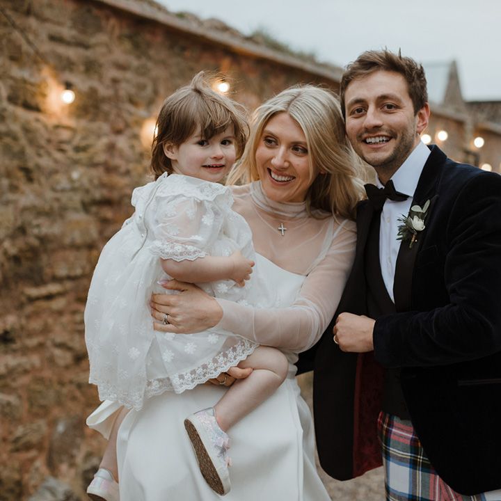 The bride and groom carry a flower girl in a white dress with white faux fur cardigan 