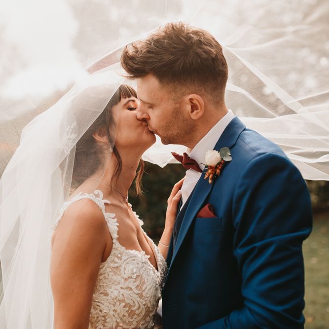 Bride and groom kissing with wedding veil blowing in the wind