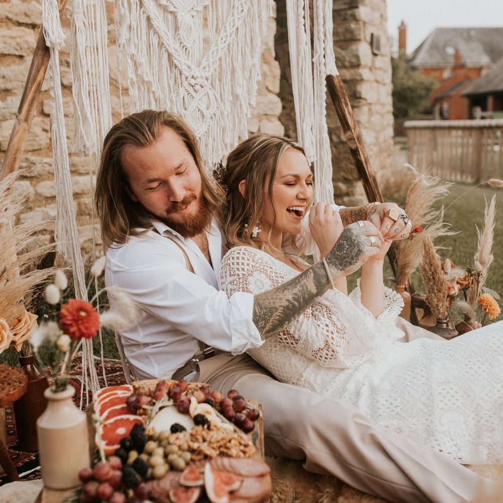 Bride & groom sit in front of Macrame backdrop for outdoor picnic