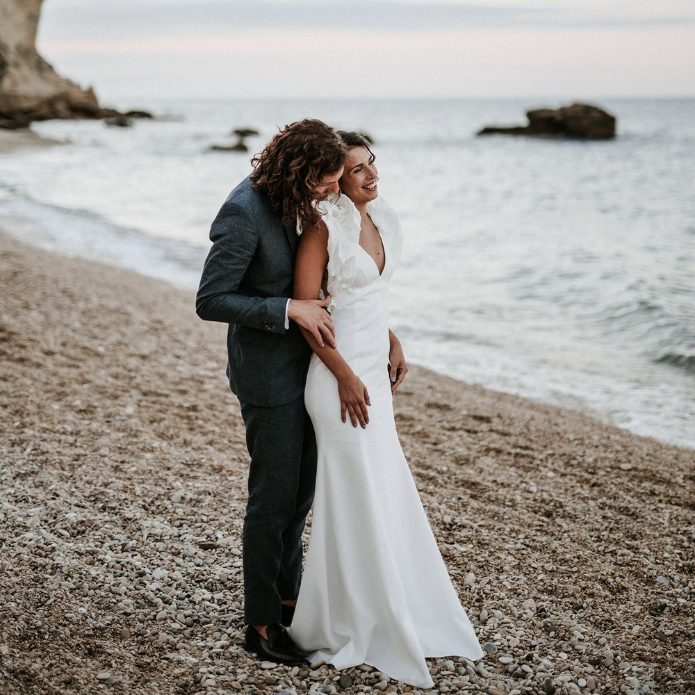 Bride and groom portrait on the beach with bride in a fitted Rime Arodaky wedding dress with ruffle sleeves and groom in a navy blue suit